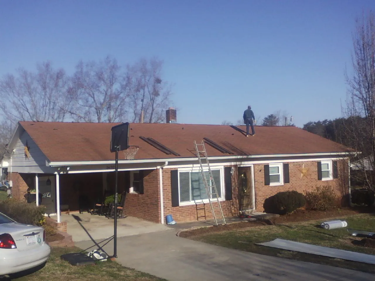 Roofer stripping a shingle roof on a brick ranch before metal panels in Newcastle