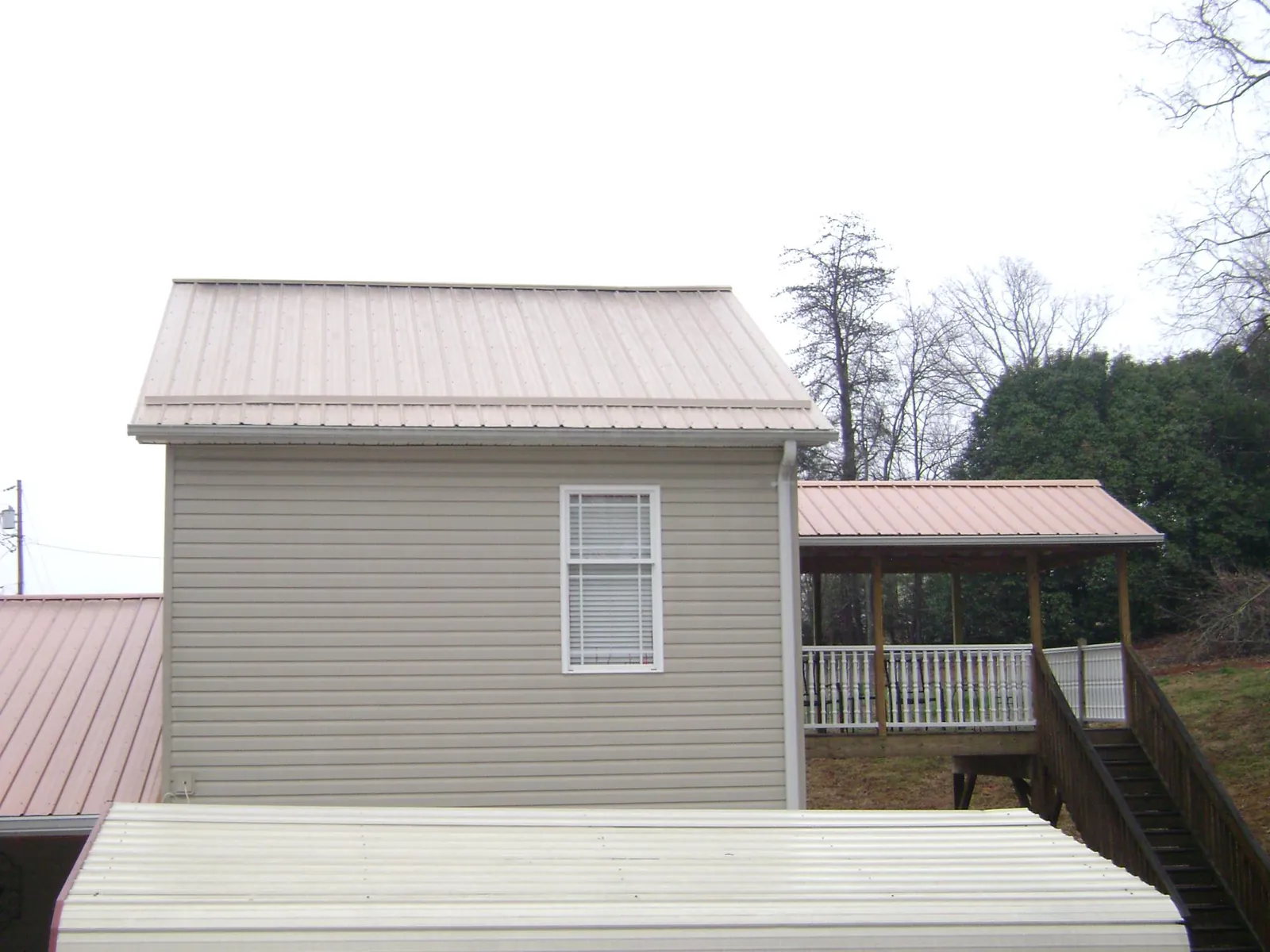 Tan metal roofs on a two story addition and attached porch, from a Roof Replacement job in Newcastle